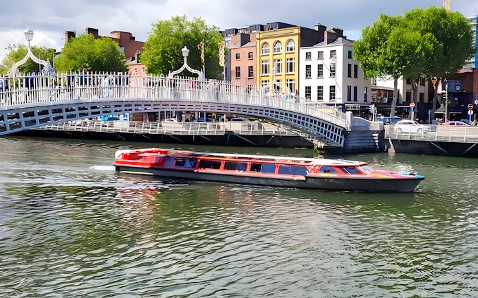 Tour boat cruising under Ha'penny Bridge on Dublin River.