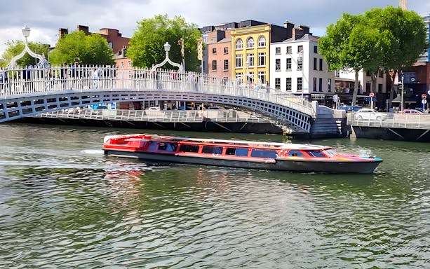 Tour boat cruising under Ha'penny Bridge on Dublin River.