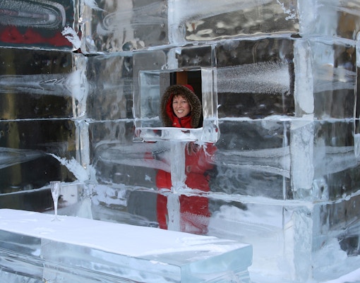 Ice bar with glass blocks and a person in a red coat peeking through a window.