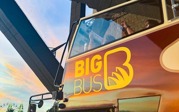 Open-top bus on Sydney night tour under bridge at sunset.
