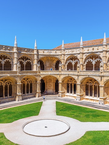 Cloister of the Monastery of Jerónimos in Lisbon, Portugal, showcasing ornate arches and manicured lawn.