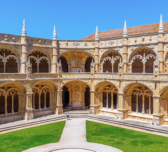 Cloister of the Monastery of Jerónimos in Lisbon, Portugal, showcasing ornate arches and manicured lawn.