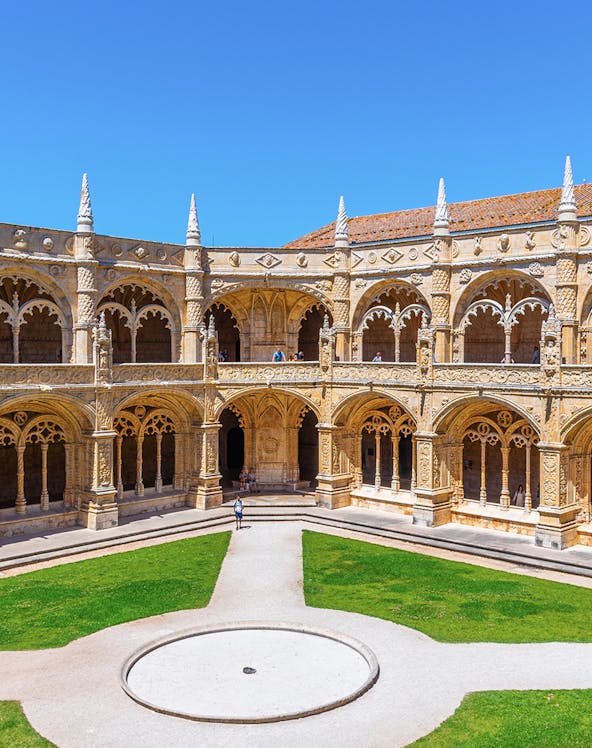 Cloister of the Monastery of Jerónimos in Lisbon, Portugal, showcasing ornate arches and manicured lawn.