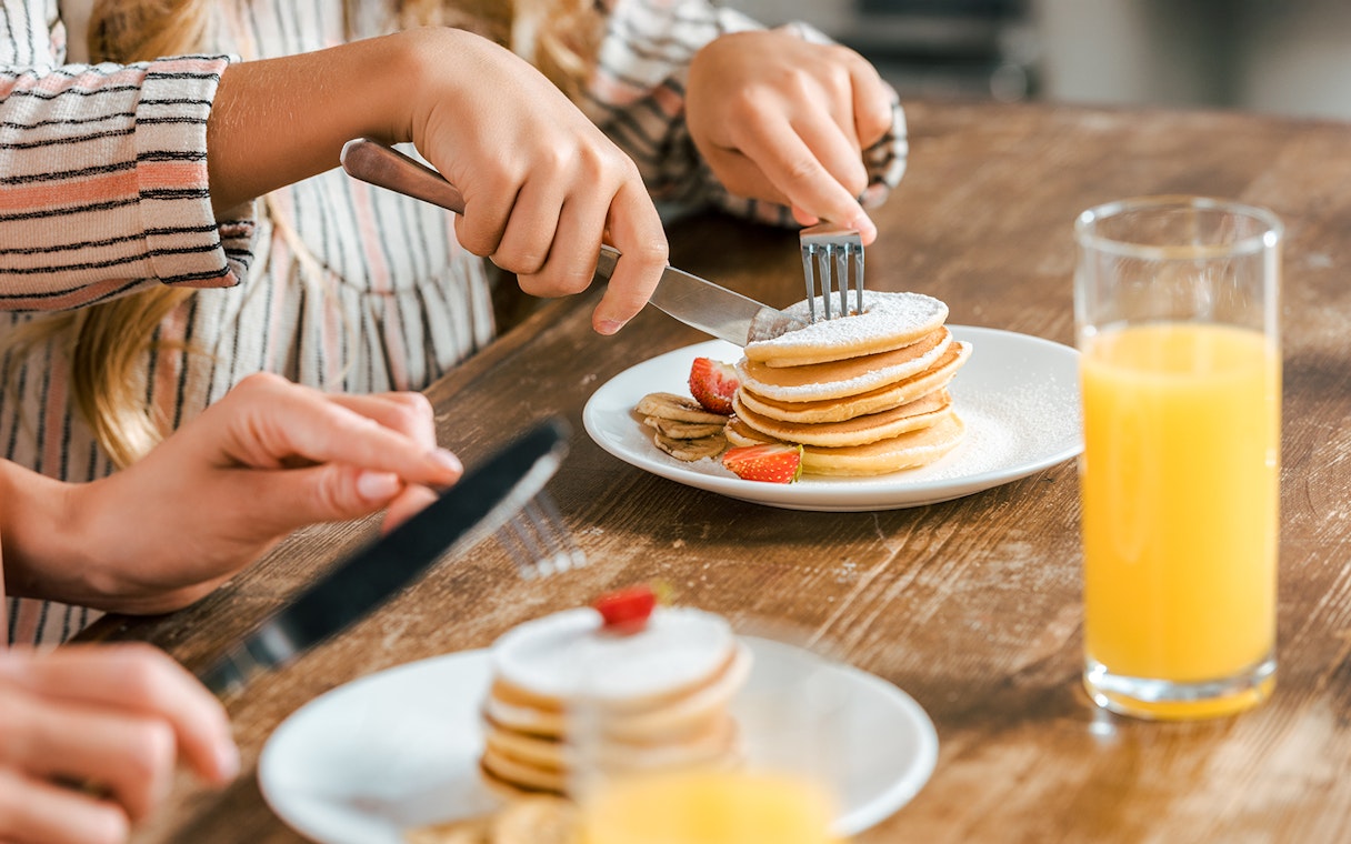 Pancakes with strawberries and bananas on a plate, close up with orange juice.