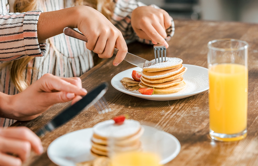 Pancakes with strawberries and bananas on a plate, close up with orange juice.