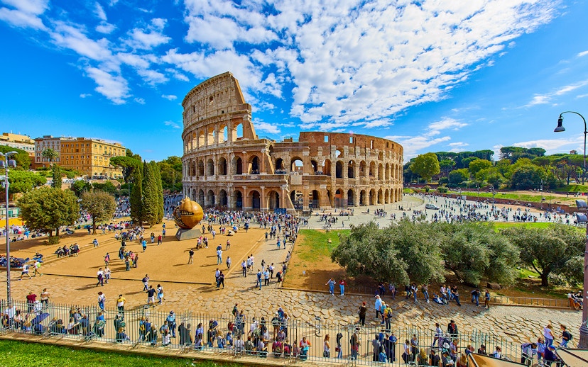 Colosseum in Rome with tourists exploring the area, viewed from a distance.