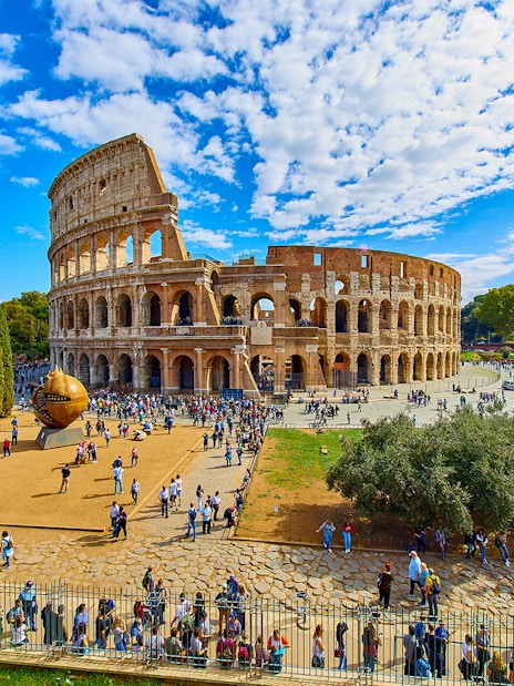 Colosseum in Rome with tourists exploring the area, viewed from a distance.