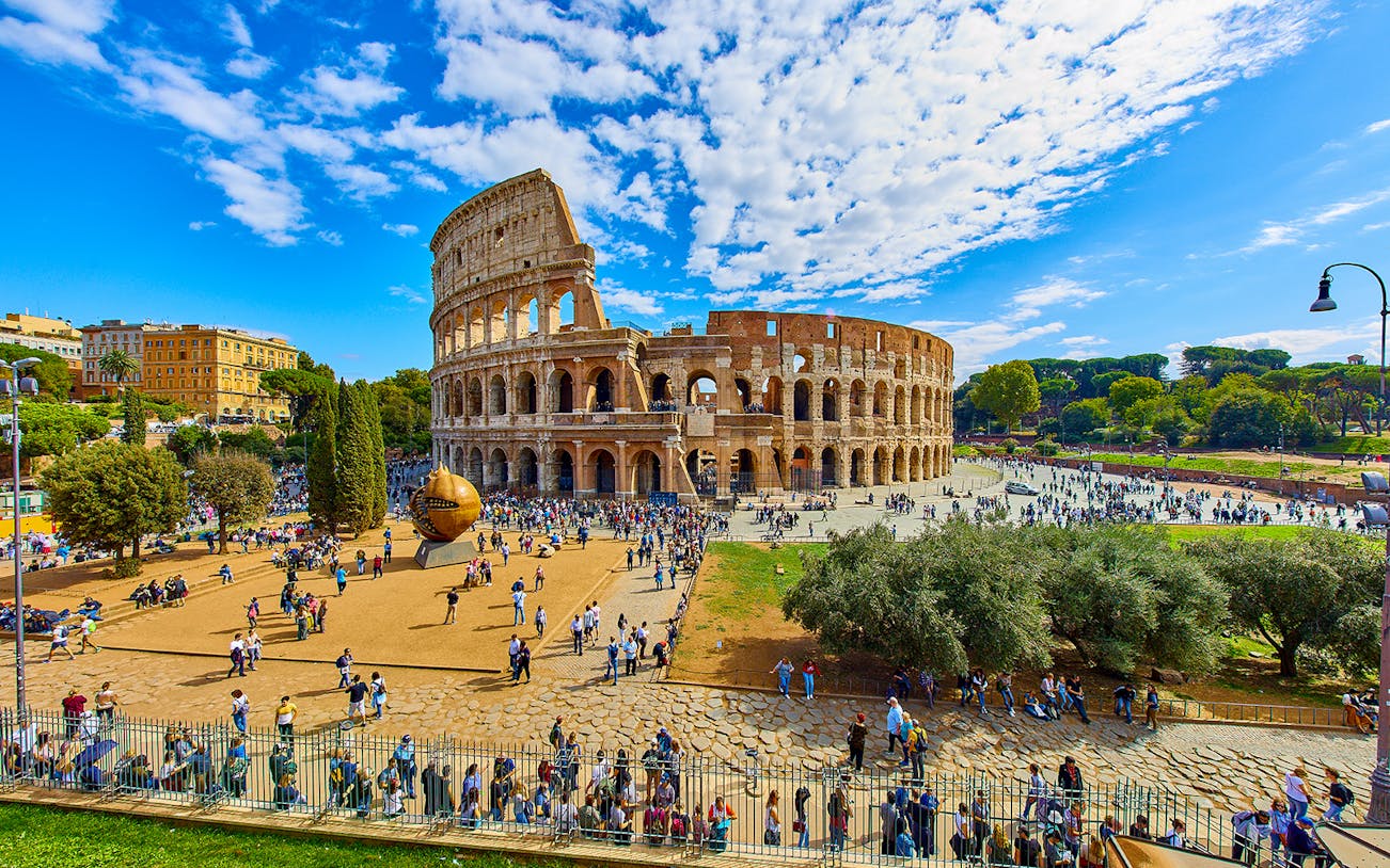 Colosseum in Rome with tourists exploring the area, viewed from a distance.