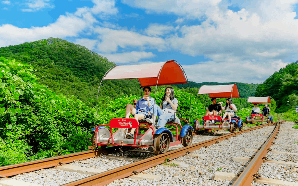 Couple enjoying Gangchon Gimnyujeong Rail Bike ride through lush greenery.
