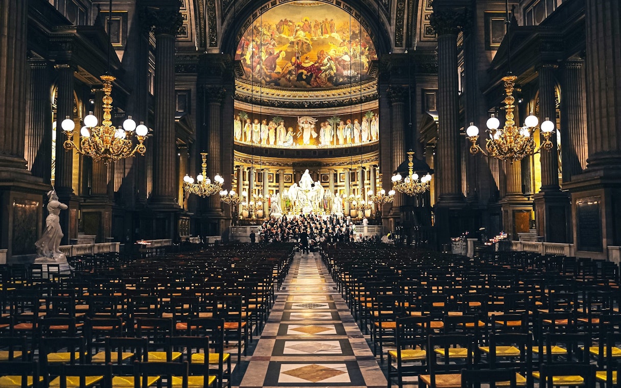 Orchestra performing in The Church of St Madeleine, Paris, France, with ornate interior and chandeliers.