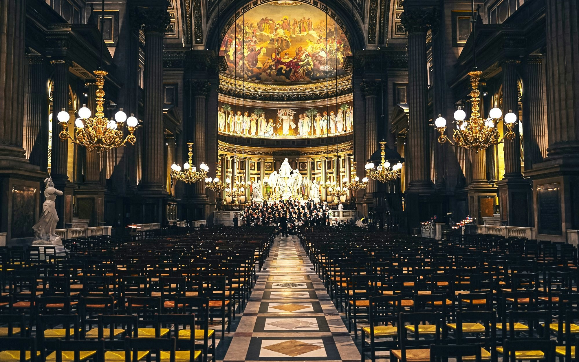 Orchestra performing in The Church of St Madeleine, Paris, France, with ornate interior and chandeliers.