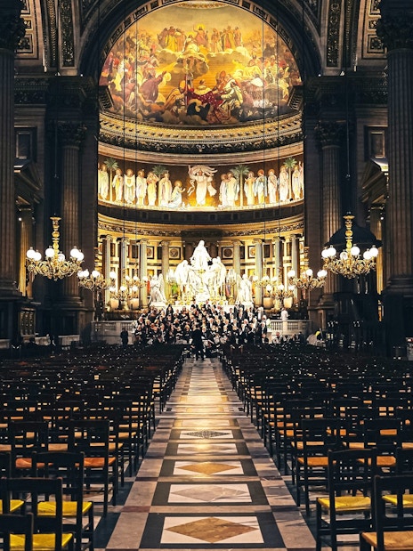 Orchestra performing in The Church of St Madeleine, Paris, France, with ornate interior and chandeliers.