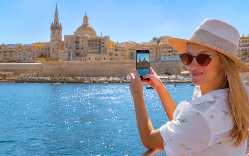 Woman photographing Valletta skyline from a boat on the Sliema Harbour Cruise.