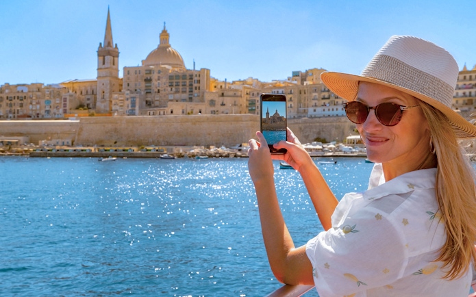 Woman photographing Valletta skyline from a boat on the Sliema Harbour Cruise.