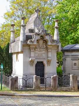 Mausoleum with ornate carvings at Père Lachaise Cemetery, Paris, surrounded by trees.