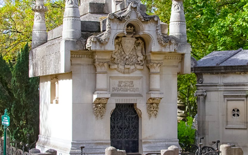 Mausoleum with ornate carvings at Père Lachaise Cemetery, Paris, surrounded by trees.