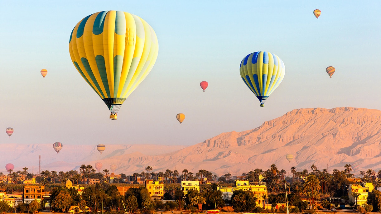 Hot air balloons over Luxor with Nile River and desert landscape.
