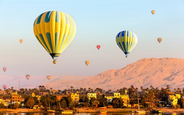 Hot air balloons over Luxor with Nile River and desert landscape.