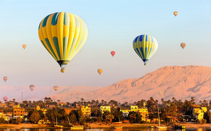 Hot air balloons over Luxor with Nile River and desert landscape.