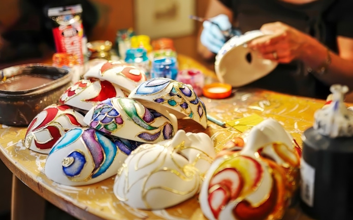 Colorful masks being painted at a workshop table with various paints and brushes.