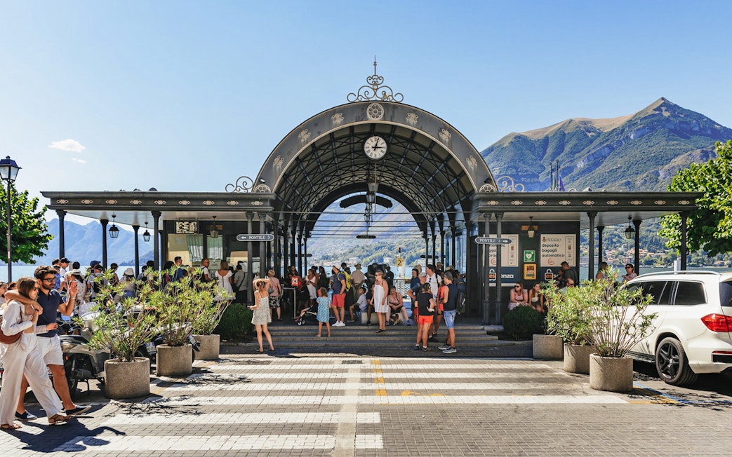 Dock of Bellagio with tourists gathering under an ornate archway, Lake Como in the background.