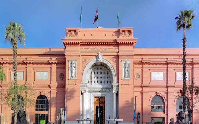 Egyptian Museum entrance in Cairo with statues and palm trees.