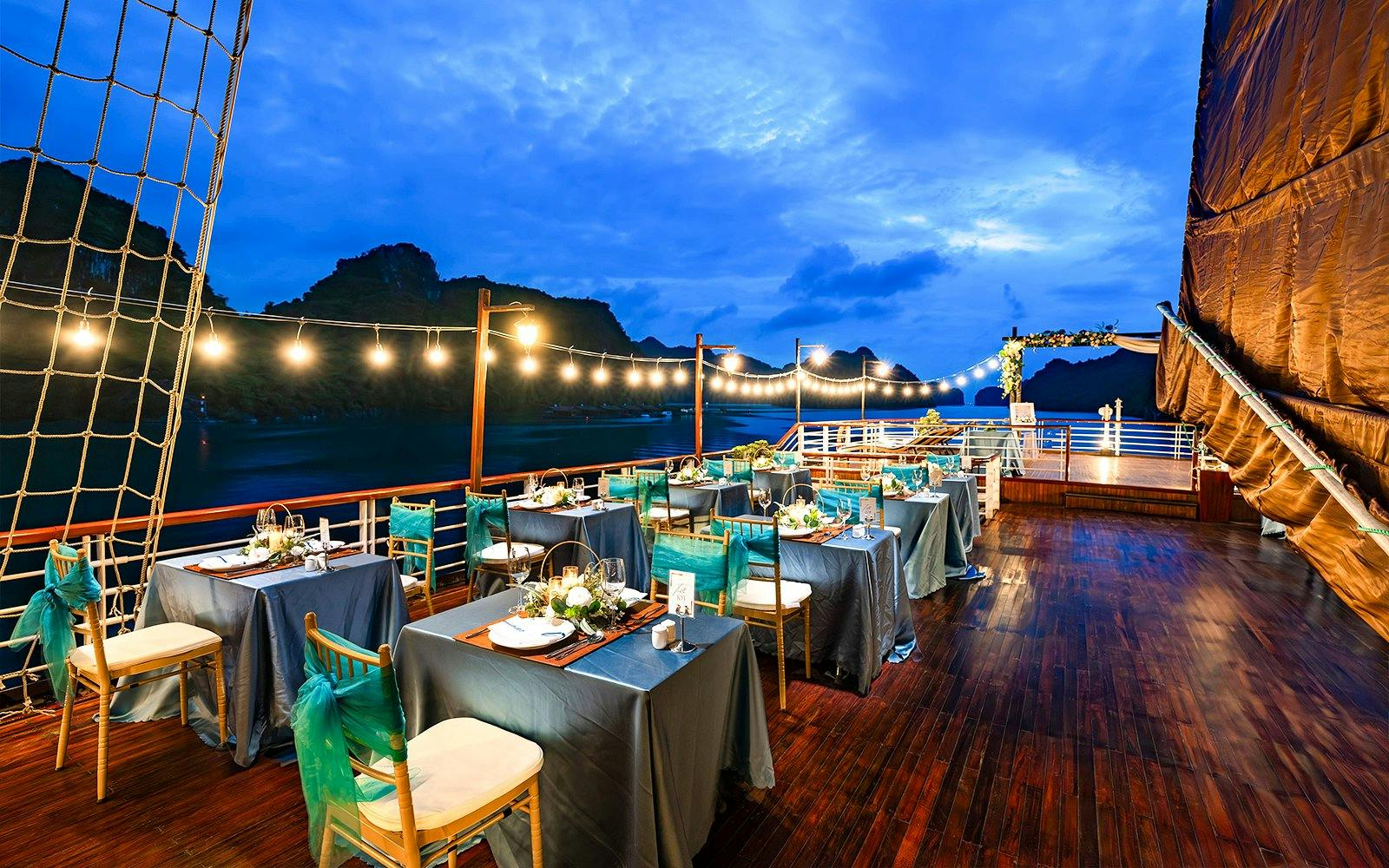 Dinner setup on outdoor deck with string lights and ocean view.