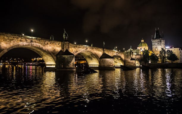 Charles Bridge illuminated at night during a boat party on the Vltava River, Prague.