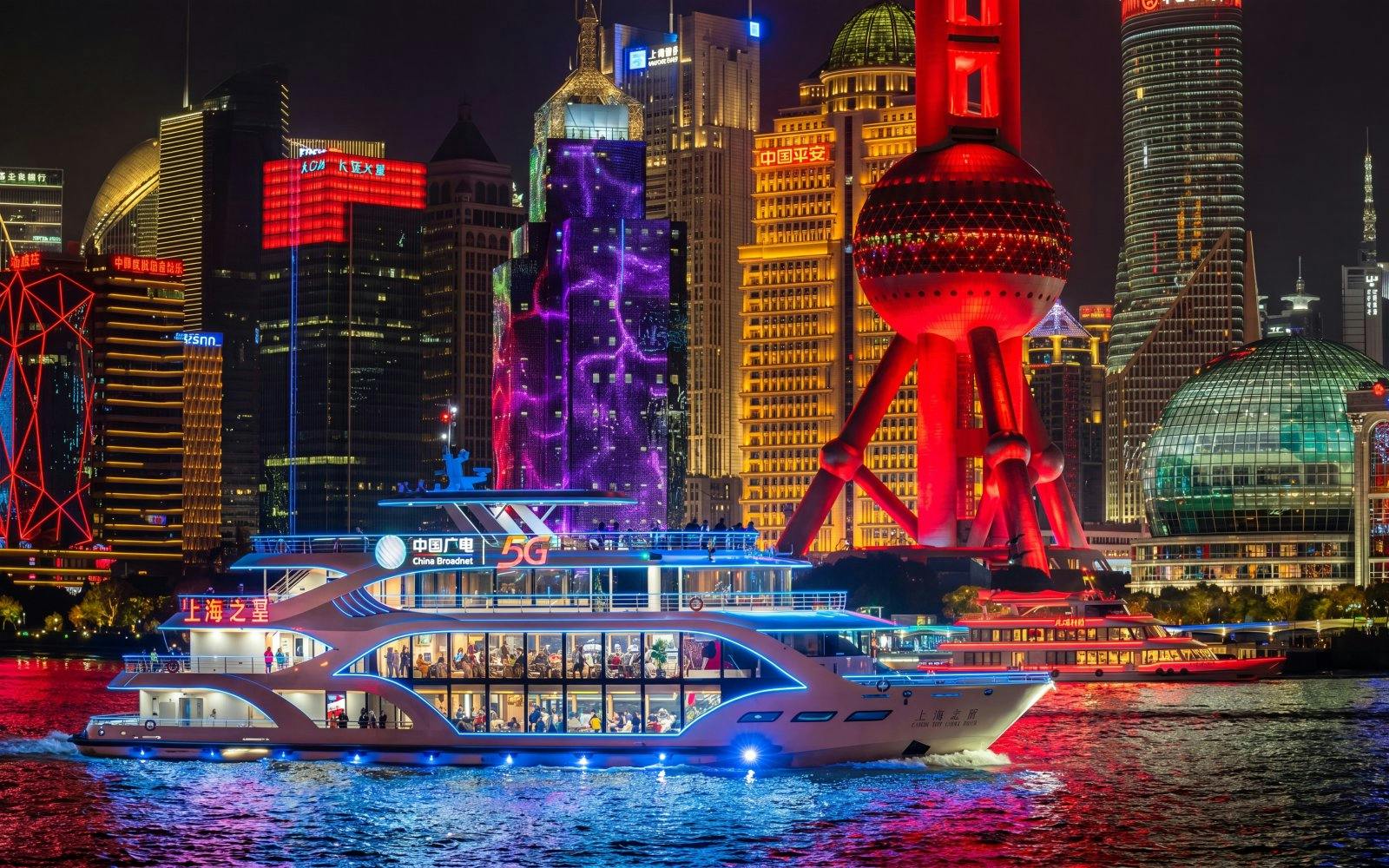 Boat cruising on Huangpu River with Shanghai skyline and Oriental Pearl Tower illuminated.