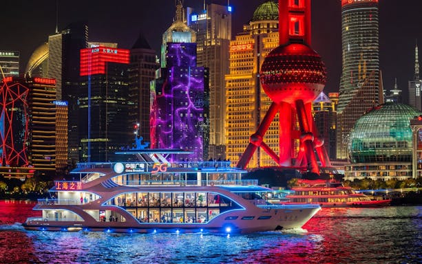Boat cruising on Huangpu River with Shanghai skyline and Oriental Pearl Tower illuminated.