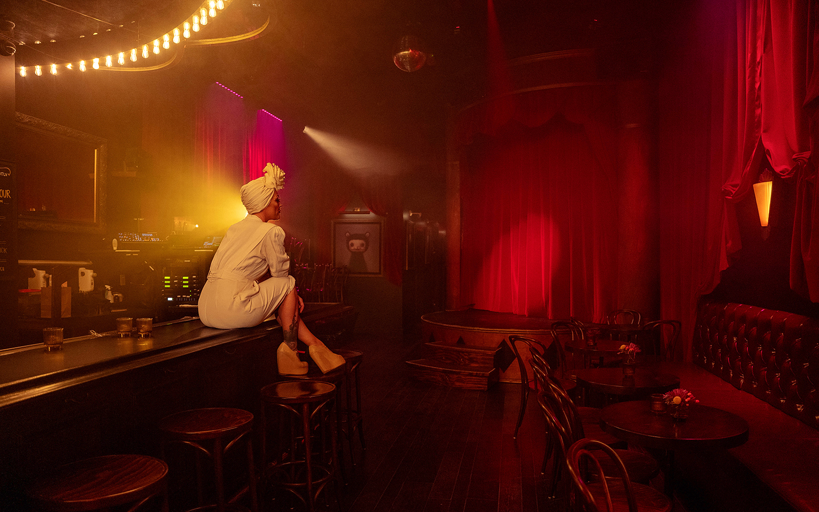 Performer sitting on bar counter in dimly lit theater for Miss Behaves: Maverick's Variety Show.