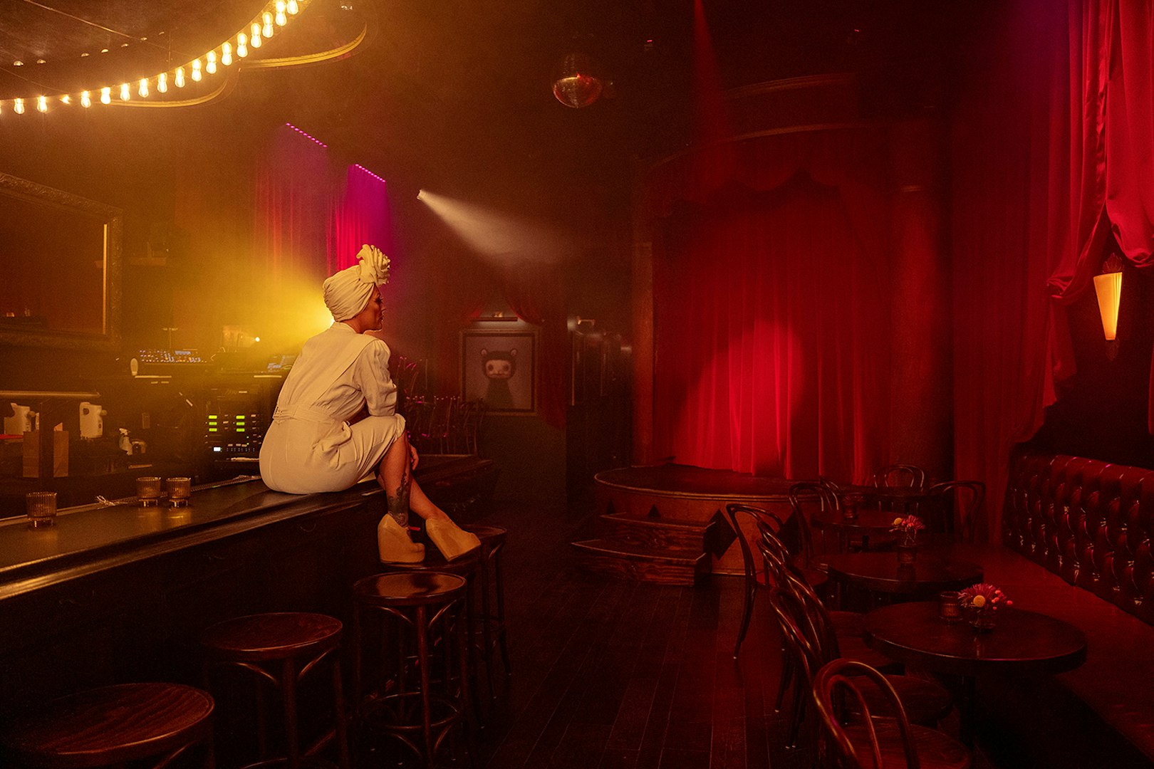 Performer sitting on bar counter in dimly lit theater for Miss Behaves: Maverick's Variety Show.