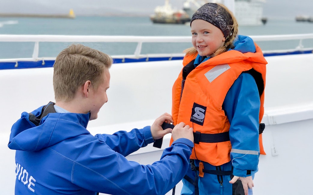 Guide assisting child with safety gear on Akureyri Whale Watching tour, Iceland.