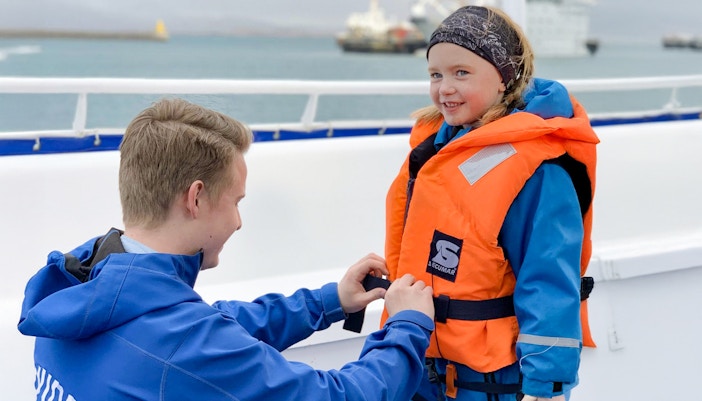 Guide assisting child with safety gear before Akureyri Whale Watching tour in Iceland.