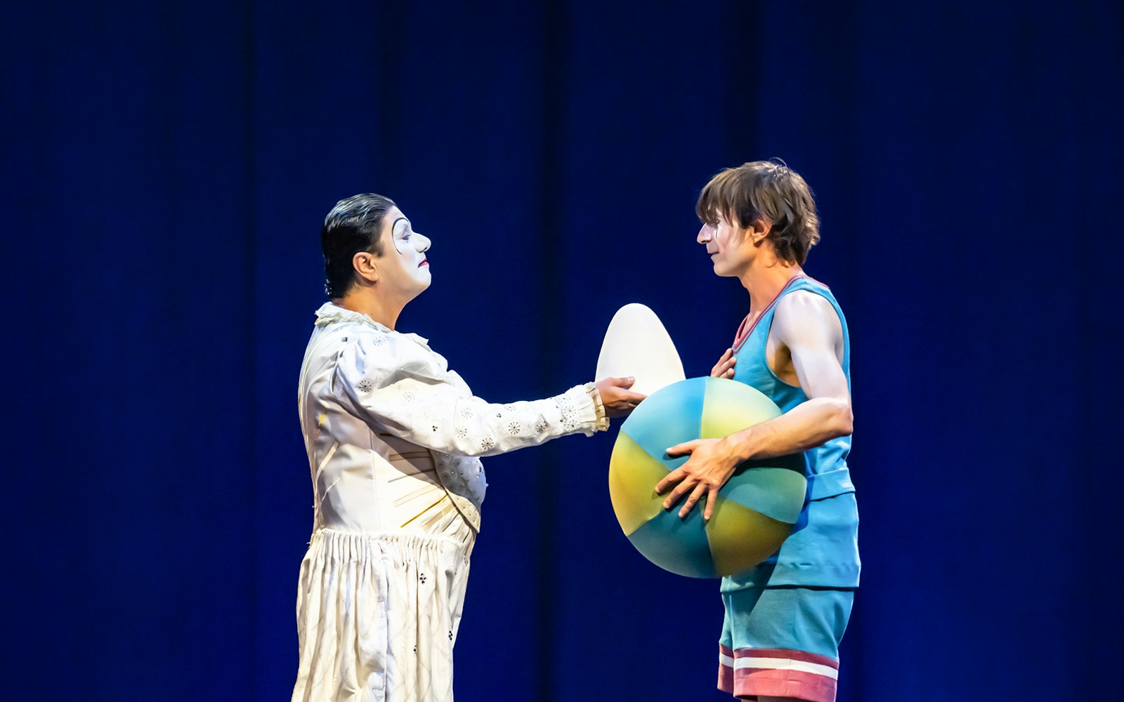 Performer in white costume interacts with another holding a colorful ball at Cirque du Soleil: Corteo.