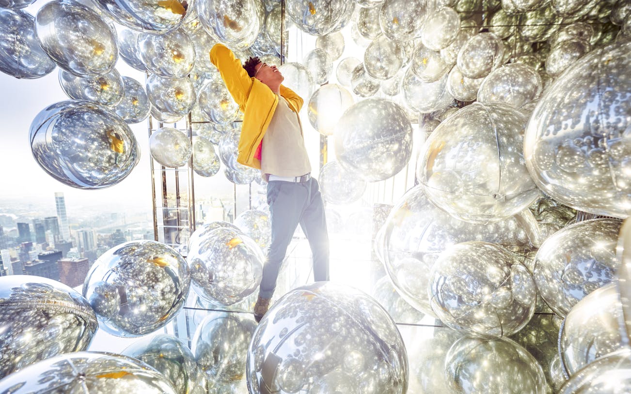 Person inside Air exhibit at SUMMIT One Vanderbilt, surrounded by reflective spheres, New York City.