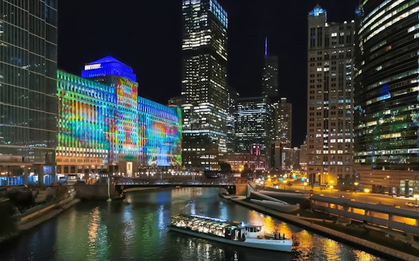 Dinner cruise boat on Chicago River with city skyline and illuminated Merchandise Mart.