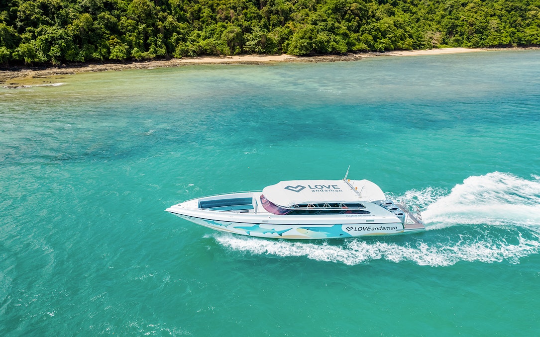 Speed boat cruising towards Similan Island with lush coastline in the background.