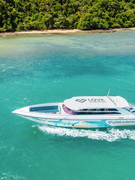 Speed boat cruising towards Similan Island with lush coastline in the background.
