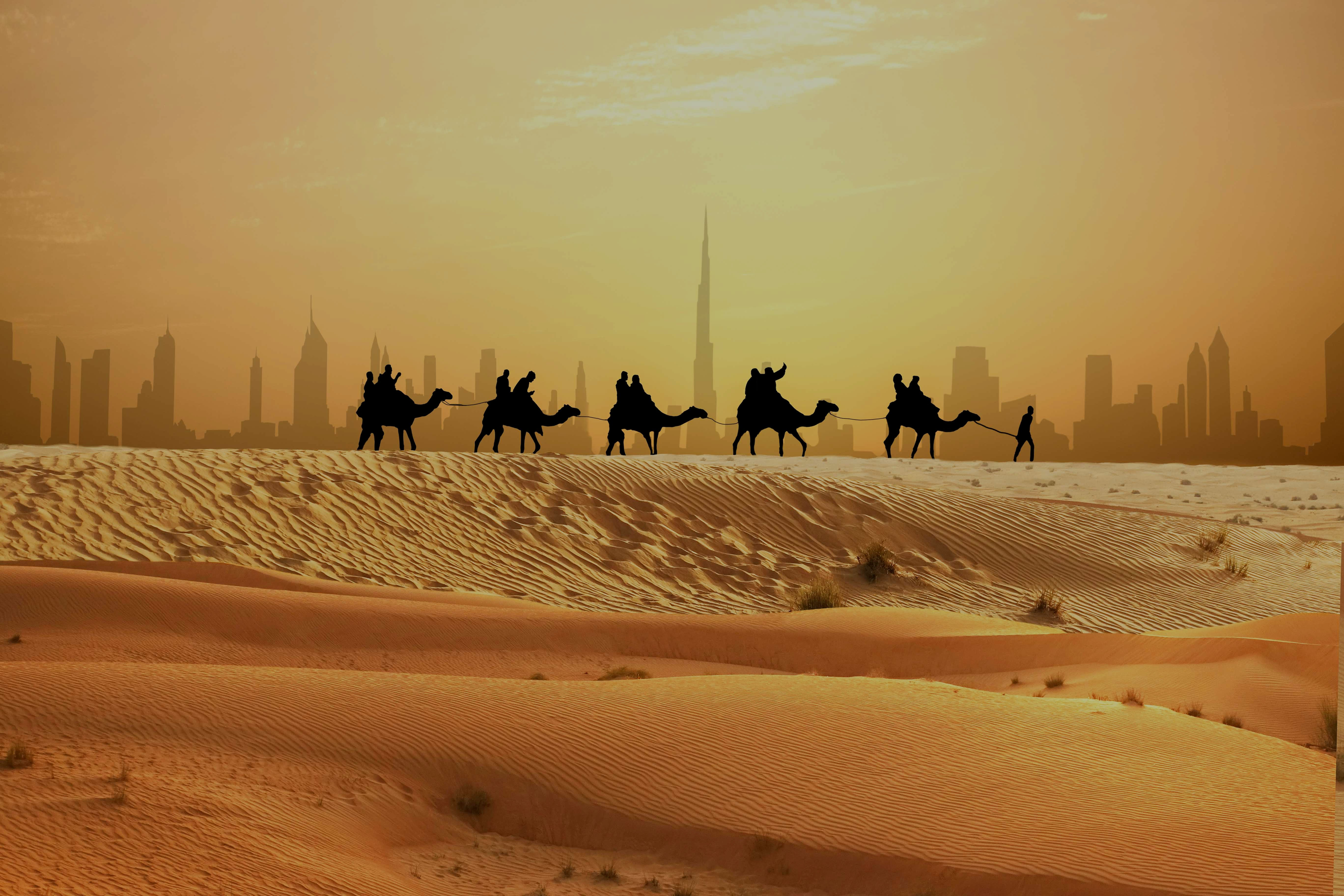 Camel caravan in Dubai desert with Burj Khalifa skyline in the background.