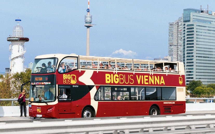 Tourists on Big Bus Vienna with Ferris Wheel and Danube River Cruise in background.