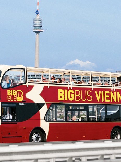 Tourists on Big Bus Vienna with Ferris Wheel and Danube River Cruise in background.