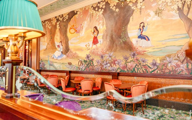 Disneyland World of Frozen Adventure restaurant with mural of princesses and elegant seating.