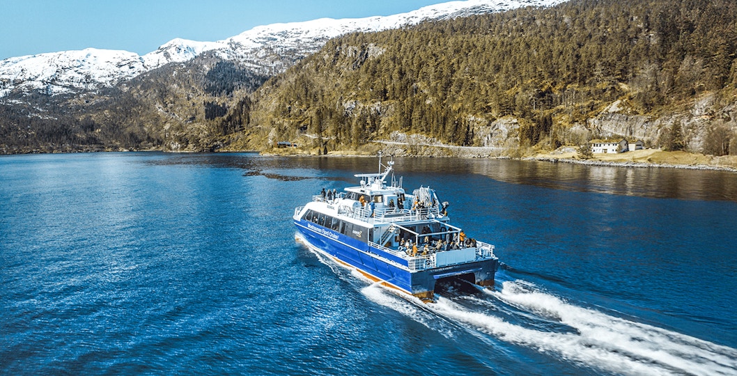 Cruise ship sailing through Mostraumen Fjord with snowy mountains in the background.