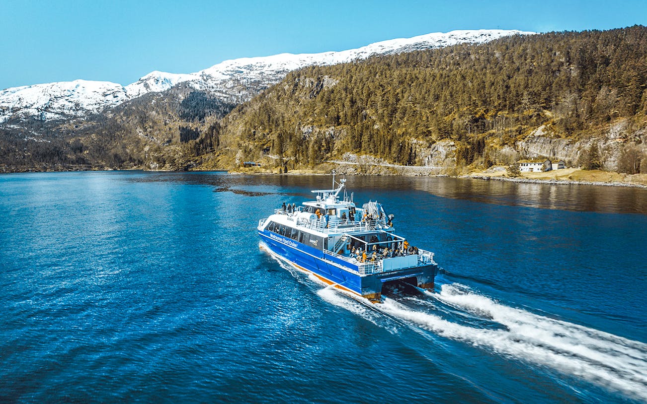 Cruise ship sailing through Mostraumen Fjord with snowy mountains in the background.