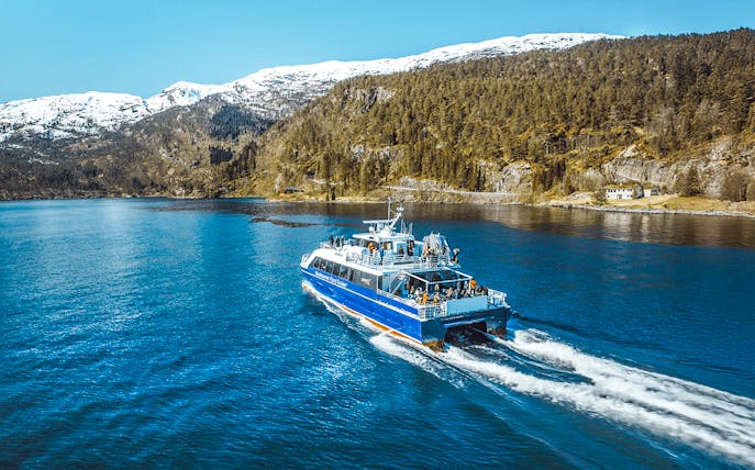 Cruise ship sailing through Mostraumen Fjord with snowy mountains in the background.