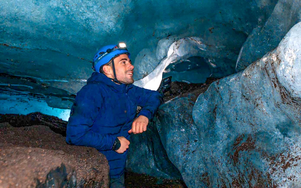 Man exploring inside a blue crystal ice cave wearing a helmet with a headlamp.