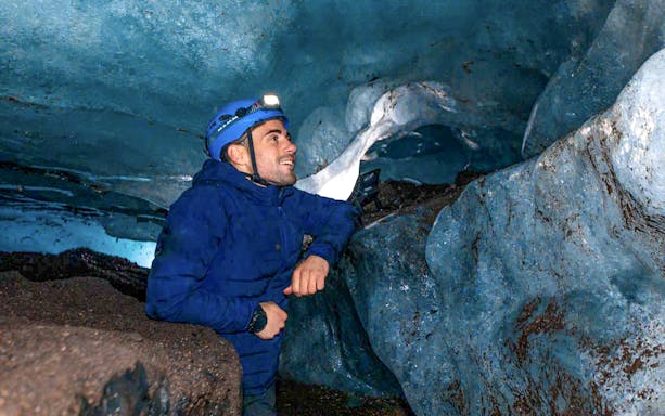 Man exploring inside a blue crystal ice cave wearing a helmet with a headlamp.