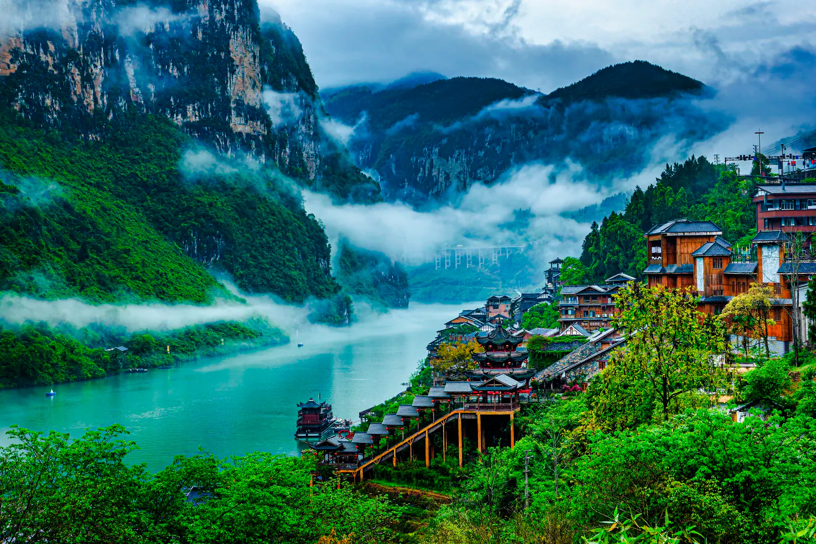 Chongqing river view with traditional wooden buildings and misty mountains.