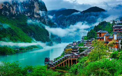 Chongqing river view with traditional wooden buildings and misty mountains.